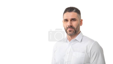 A man with a short beard and trimmed hair is standing against a plain white background, wearing a white button-up shirt. He has a neutral expression, panorama with copy space