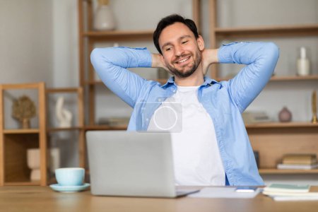 Photo for A content man leans back in his chair in a well-lit home office, his hands behind his head, expressing satisfaction and taking a break in front of his laptop, surrounded by notes and a cup of coffee. - Royalty Free Image