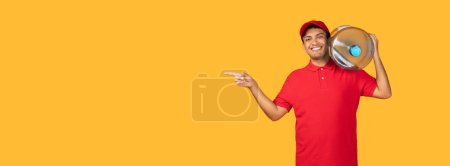 Delivery man wearing a red uniform is standing over yellow studio background while holding a large bottle of water in his hand, panorama with copy space