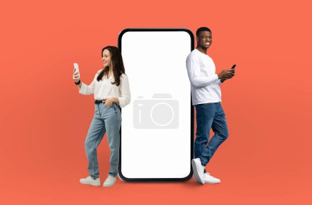 Téléchargez les photos : Un homme et une femme sont positionnés à côté d'un écran blanc sur un fond orange. Ils sont debout et semblent se concentrer sur l'écran vide devant eux. - en image libre de droit