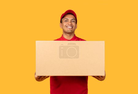 A man wearing a red shirt is seen grasping a cardboard box in his hands. The man appears to be standing upright, firmly holding onto the box with a focused expression on his face.