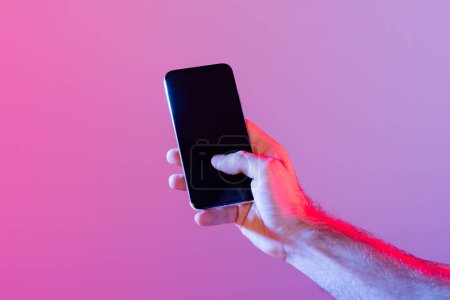 Una persona sostiene un teléfono inteligente con una pantalla oscura y sin iluminación sobre un fondo púrpura degradado. La iluminación arroja un brillo suave y ambiental, creando un ambiente moderno y conocedor de la tecnología.