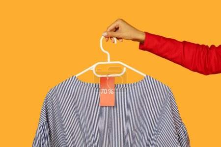 Una persona está sosteniendo una camisa en una percha, mostrando la etiqueta de precio adjunta a ella. La camisa aparece cuidadosamente exhibida y lista para la compra, recortada