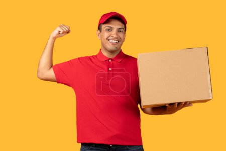 A cheerful delivery worker man in a red cap and polo shirt holds a cardboard box while flexing his arm, showing enthusiasm and strength.
