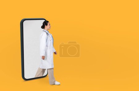 A medical professional lady dressed in a white lab coat and stethoscope walks through a large smartphone frame against a vibrant yellow background, the concept of telemedicine or digital healthcare.