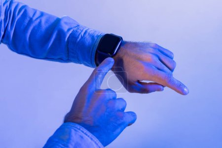 Der Mensch interagiert mit seiner Smartwatch, indem er mit dem Finger durch Benachrichtigungen oder Optionen navigiert. Das umgebende blaue Licht verleiht der Szene ein futuristisches und modernes Flair, beschnitten