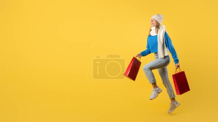 Eine Frau im blauen Pullover steht da und hält Einkaufstüten in der Hand. Sie scheint in einem Einkaufsviertel mit Geschäften um sich herum zu sein. Der weibliche Ausdruck ist nicht sichtbar, Kopierraum