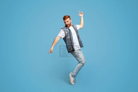Junger fröhlicher stilvoller Mann, der auf Zehenspitzen auf blauem Studiohintergrund tanzt, Kopierraum, Aufnahme in voller Länge