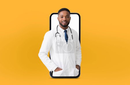 El médico afroamericano con un estetoscopio, con una bata blanca de laboratorio y una corbata azul, emerge de la pantalla de un teléfono inteligente, simbolizando la telemedicina sobre un vibrante telón de fondo amarillo.