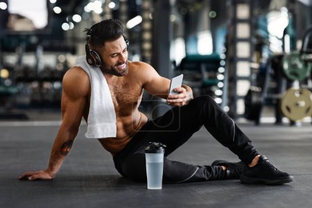 Online personal trainer on mobile phone. Muscular man using cellphone at gym, free space