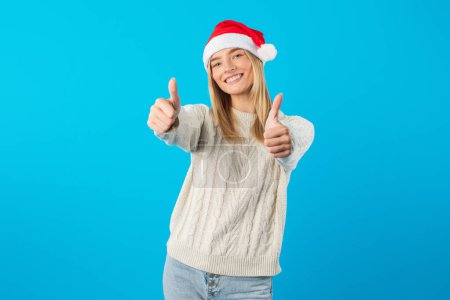 A woman wearing a Santa hat is smiling and giving a thumbs up gesture. She appears to be in a festive mood, showcasing positivity and approval.
