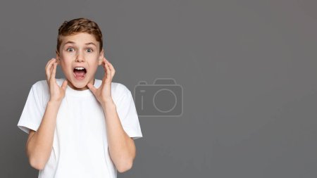Ein begeisterter Teenager mit den Händen vor dem Gesicht und weiten Augen, isoliert auf einem grauen Hintergrund, mit schockiertem Gesichtsausdruck, Kopierraum