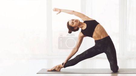 A young woman is engaged in a serene yoga session inside a well-lit studio, demonstrating flexibility and focus while performing the Extended Side Angle Pose