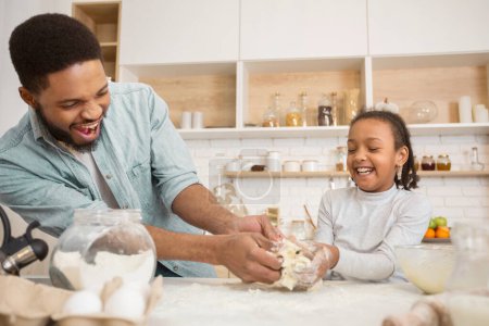 Padre e hija afroamericanos disfrutan haciendo pasteles, compartiendo una risa en un momento de vinculación de la cocina y conexión familiar
