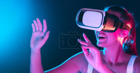 Une femme porte un casque de réalité virtuelle, pleinement engagé dans un monde numérique. Le casque couvre ses yeux et ses oreilles, tandis qu'elle explore un environnement simulé à travers des gestes de main