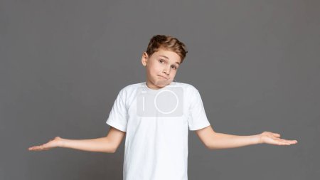 Un adolescente se encuentra aislado sobre un fondo gris, expresando incertidumbre al encogerse de hombros con las palmas abiertas