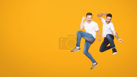 Duo of european men captured mid-jump against orange backdrop, encapsulating the essence of friendship and camaraderie among mates