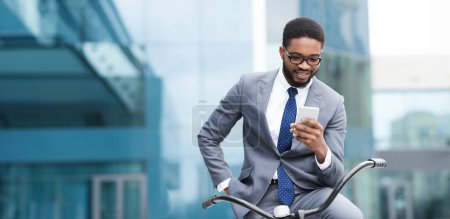 Un hombre negro profesional está al aire libre con su bicicleta, usando su teléfono. El escenario es tranquilo y urbano, reflejando un equilibrio entre los deberes profesionales y las actividades de ocio.