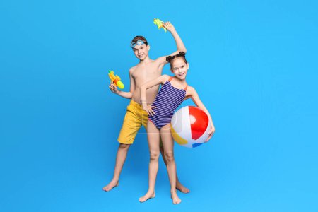 Happy summer holidays. Cheerful boy and girl playing with beach toys, blue studio background