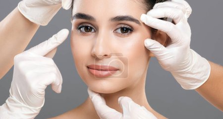 Mediziner mit Handschuhen beurteilen die Gesichtshaut einer Frau, indem sie verschiedene Bereiche sanft berühren und untersuchen. Der Fokus liegt auf ihrem klaren und strahlenden Teint.