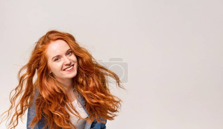 A woman with vibrant red hair is smiling happily. Her long hair cascades down her shoulders as she beams with joy, copy space