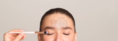 Eine Frau schminkt ihre Augen mit einem Pinsel. Sie bürstet sorgfältig jedes Augenlid, um einen klar definierten und gepflegten Look zu erzielen..