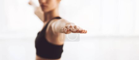 Eine Person praktiziert Yoga in einem hellen, luftigen Raum. Das Individuum befindet sich in einer fokussierten Haltung und streckt die Arme nach außen, was darauf hindeutet, dass es sich in einer ausgleichenden Pose befindet.