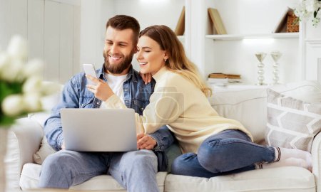 Surfing Internet. Young Couple Relaxing With Laptop And Smartphone, Sitting On Sofa