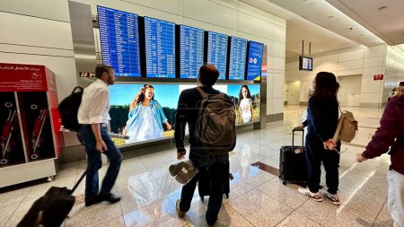Photo for DUBAI,UNITED ARAB EMIRATES.15 SEPTEMBER 2023.Man with luggage, walking in Dubai Airport, checking flight info board - Royalty Free Image