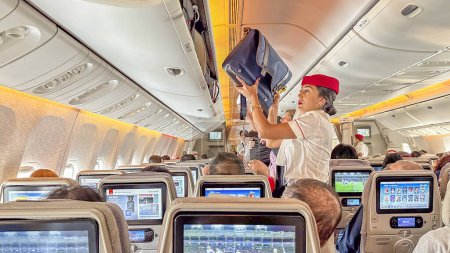 Photo for DUBAI,UAE. 16 SEPTEMBER 2023. Passenger seated, stewardess stows baggage, a seamless start to the airborne voyage - Royalty Free Image