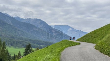 Photo for DOLOMITES,ITALY. 17 SEPTEMBER 2023.Santa Maddalena, Val di Funes. Serpentine hill road meanders through vibrant greens, two hikers at its end-a snapshot of Alpine beauty in the heart of nature - Royalty Free Image