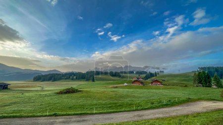 Photo for A verdant alpine pasture dotted with Italian houses, with the stunning Alpe di Siusi mountain ridge in the backdrop of the Dolomites - Royalty Free Image