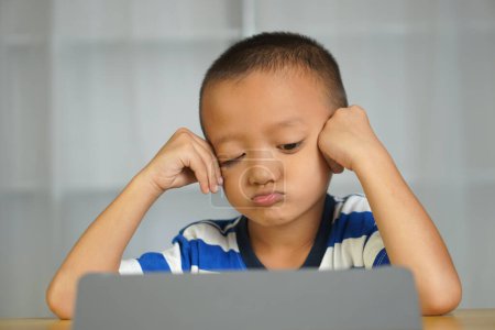 Téléchargez les photos : Un garçon s'ennuie parce qu'il regarde l'ordinateur depuis longtemps. - en image libre de droit