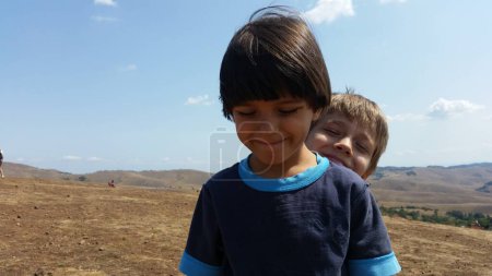 Téléchargez les photos : Enfants heureux debout sur le champ vert, le jour ensoleillé.. Garçons Summer photo. Paysage montagne - en image libre de droit
