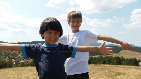 Téléchargez les photos : Les enfants heureux debout sur le champ vert avec les mains sages, le jour ensoleillé. Garçons Summer photo. Paysage montagne - en image libre de droit