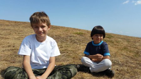 Téléchargez les photos : Joyeux enfants assis sur le terrain vert, le jour ensoleillé.. Garçons Summer photo. Paysage montagne - en image libre de droit