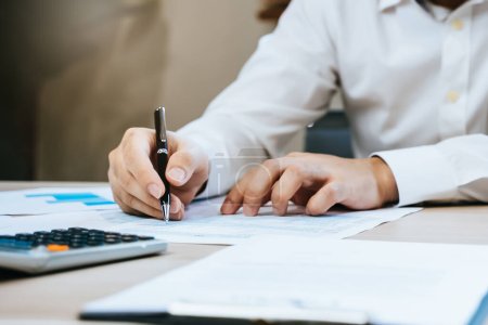 De cerca la mano del contador profesional revisa el papeleo fiscal y firma la firma sobre la mesa en el lugar de trabajo