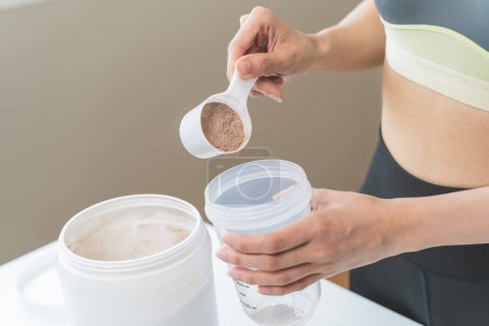 Young sporty woman pouring protein powder into a cup to make replacement food meal after workout