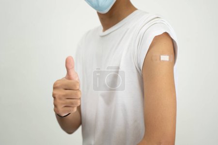 Foto de Feliz hombre asiático mostrando su brazo y vendaje después de recibir una vacuna. - Imagen libre de derechos