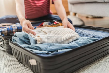 Foto de Preparando la maleta para el viaje de vacaciones de verano. Mujer joven revisando accesorios y cosas en el equipaje en la cama en casa antes de viajar. - Imagen libre de derechos