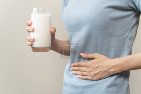 concepto de intolerancia a la lactosa. Mujer sosteniendo un vaso de leche y con dolor de estómago.