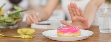 Photo for Woman on dieting for good health concept. Close up female using hand push out her favourite donut and choose salad vegetables for good health. - Royalty Free Image