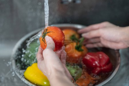 Großaufnahme von Händen, die Gemüse mit Leitungswasser an der Spüle in der Küche waschen, um Zutaten für einen frischen Salat zu reinigen.