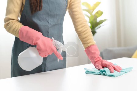 Foto de Trabajadora de servicio ama de llaves feliz limpiando la superficie de la mesa por producto más limpio para limpiar el polvo. - Imagen libre de derechos