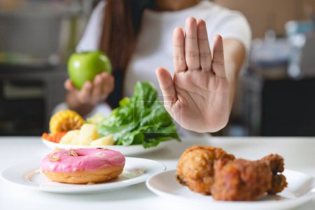 Téléchargez les photos : Woman on dieting for good health concept. Close up female using hand push out her favourite donut and choose green apple and vegetables for good health. - en image libre de droit