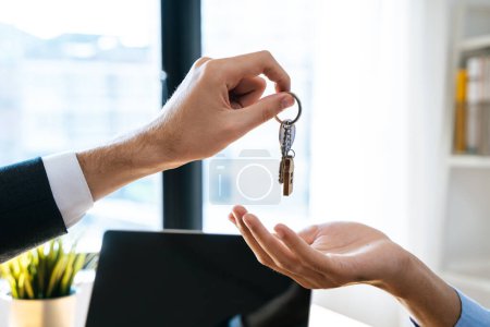 Téléchargez les photos : Vue rapprochée main de l'agent immobilier propriétaire donnant maison clé à l'acheteur locataire. - en image libre de droit