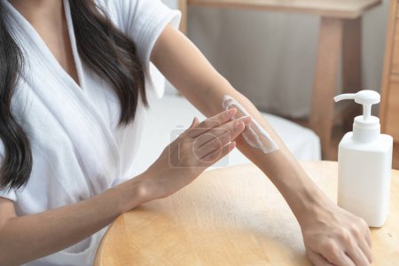 Téléchargez les photos : Young woman applying moisturizer cream to her arm in the morning routine. - en image libre de droit