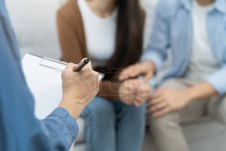 Photo for Couple relationship therapy with a counselor. Close Up hands of the psychologist take notes on a clipboard during a conversation with clients to find problems and solution. - Royalty Free Image