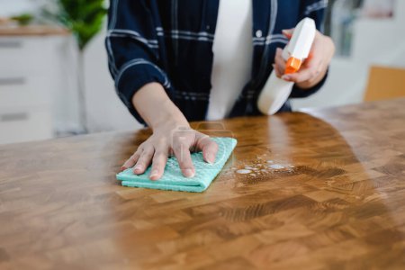Téléchargez les photos : Femme au foyer nettoyage table en bois par chiffon et solution de nettoyage - en image libre de droit