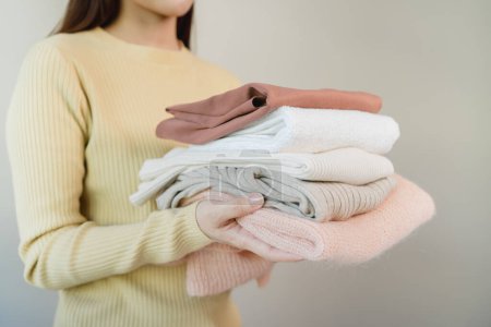 Photo for Young female holding a stack of folded clothes isolated on background - Royalty Free Image